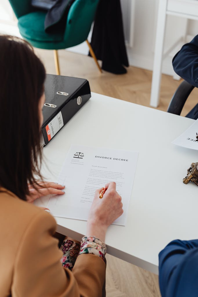 Over the shoulder view of a person signing a divorce decree at a desk in an office.