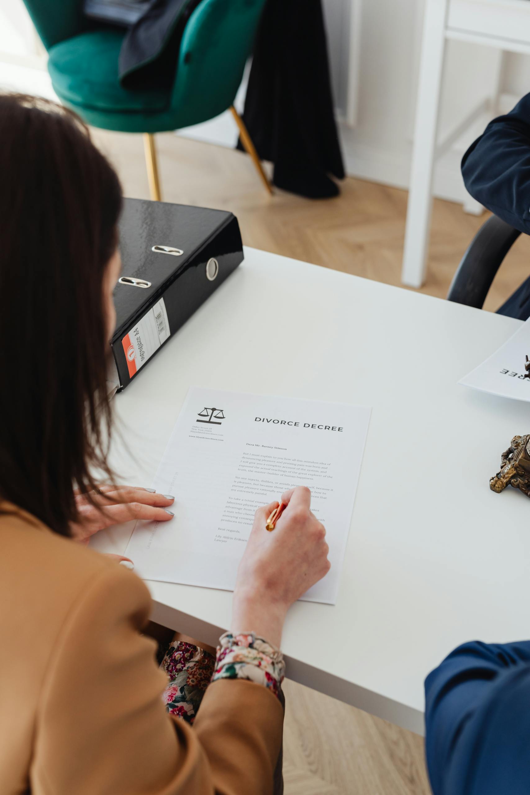 Over the shoulder view of a person signing a divorce decree at a desk in an office.